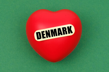 On a green surface lies a red heart with the inscription - Denmark