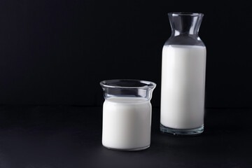 glass and jug with milk on black background