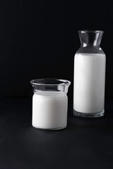 glass and jug with milk on black background