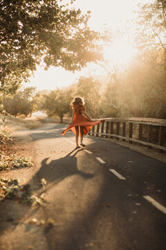 Teen girl twirling her red dress on a trail in sunset 