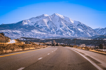 View of local Colorado highway leading to beautiful snowcapped mountain - obrazy, fototapety, plakaty