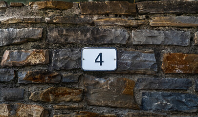 House number 4. Number 4 on a rock wall of a rural village street. Customizable house number sign.