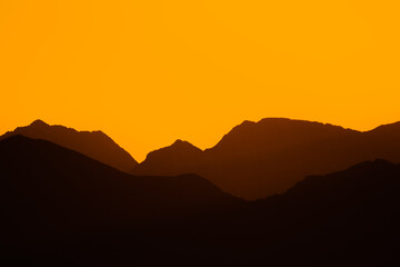 Mountain silhouette landscape at sunset or sunrise with golden hour orange colors. Real mountain silhouettes. Concept of nature, sport, travel, lifestyle.