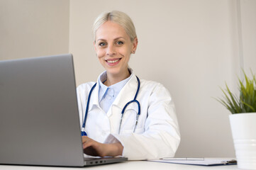 Modern tech for healthcare. Smiling female doctor sit at desk use laptop watch professional training webinar online manage electronic medical document.