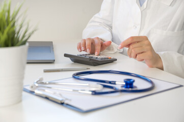 Medical insurance concept . Unrecognizable doctor or nurse with calculator at the table with stethoscope and forms