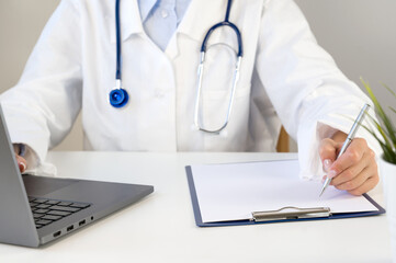 Unrecognizable female doctor in white medical uniform sit at desk doing paperwork. Healthcare concept