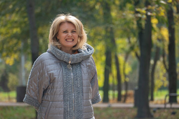 Emotional middle-aged woman in autumn park. Middle-aged blond woman on a walk. Psychological health, psychology concept.