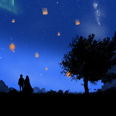 A silhouette of a couple standing near a tree watching lanterns in the blue night sky 