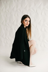 Portrait of confident woman in formal outfit posing on white background. Serious woman, with evening makeup, wearing black jacket and heels while looking at camera in the studio