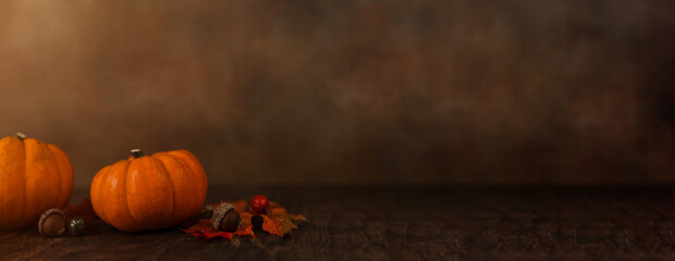 A row of miniature orange pumpkins on a rustic wood surface with a brown abstract background with...