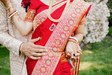 Man and woman hugging during a traditional Indian wedding. Faceless bride and groom in ceremonial costume with embroidery and gold decorations standing in the garden