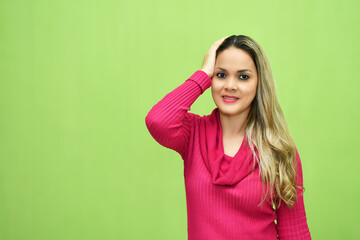 Mujer Joven Latina con la mano derecha sobre su cabeza sobre fondo verde, espacio para texto al...