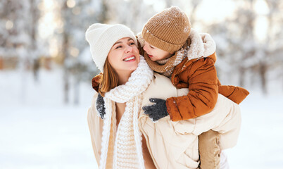 Mom giving piggyback ride to happy little son while walking outdoors in snowy winter park