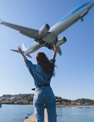 Girl and airplane in flight, landscape with woman standing with hands raised up, waving arms and flying passenger airplane, female tourist and landing commercial aircraft, summer sunny day