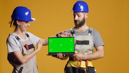 Team on builders holding laptop with greenscreen template, advertising chroma key isolated display...