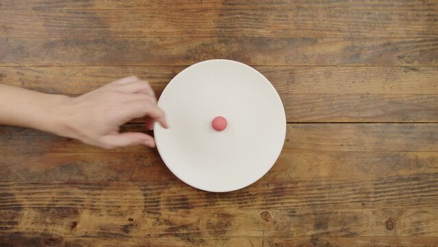 Vue de dessus d'une main de femme qui prend en h&eacute;sitant le dernier bonbon fraise dans une assiette blanche