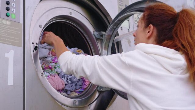 Housewife young woman do housework, busy in regular housekeeping work put towels into washing machine, turns on modern washer-dryer appliance in cozy laundry room. Household chores concept