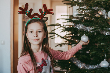 Portrait of a girl next to the New Year tree, holding a Christmas tree decoration in her hands and...
