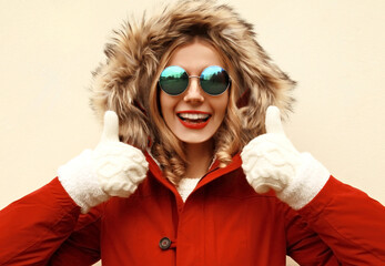 Portrait of happy surprised laughing young woman showing finger gesture thump up wearing red jacket with fur hood and mittens