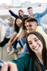Vertical shot of multiracial young group of friends having fun and laughing while taking a selfie...