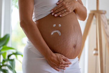 Sad smiley drawn with cream on pregnant belly with stretch marks