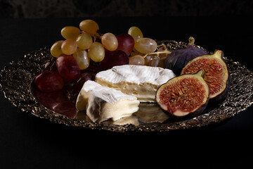 cheese, figs and grapes on a silver plate on a dark background