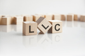text LLC on wooden blocks with letters on a white background. reflection of the caption on the mirrored surface of the table