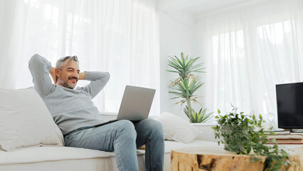 Senior mature adult man sitting on sofa using laptop on holiday.