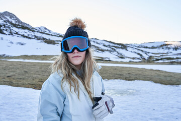 pretty girl looks at the camera with a casual and calm appearance equipped with a hat and snow goggles