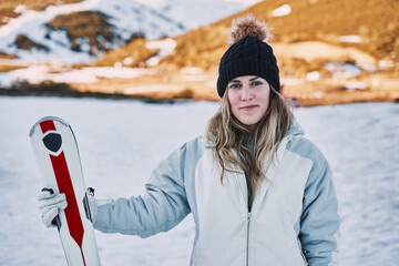 pretty girl holds some skis while looking at the camera with a slight smile.