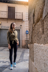 Fototapeta na wymiar Young woman traveller walking through a narrow street during a antumn afternoon looking to the camera