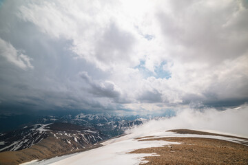 Awesome top view through clouds to high snowy mountains. Scenic landscape with beautiful snow mountains in low clouds. Atmospheric alpine view from stone hill to snow mountain range with low clouds.