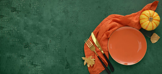 Autumn table setting with leaves and pumpkin on green background with space for text