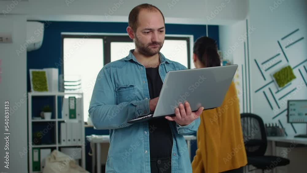Poster portrait of casual business man holding laptop typing on keyboard and smiling at camera in busy mode