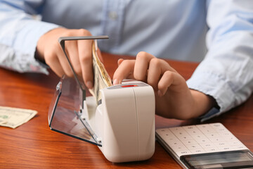 Female accountant putting money into currency counting machine on table