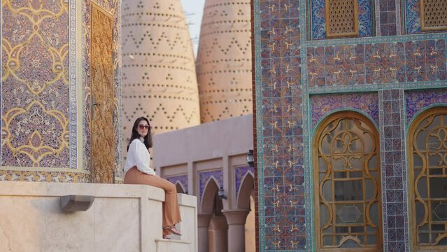 tourist woman sitted at Blue mosque of Katara village made of colorful mosaic in Doha Qatar showing Pigeon tower behind
