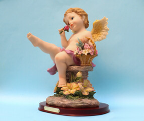 Figura de Ángel sentado disfrutando el aroma de una flor. 