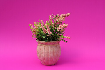 Maceta pequeña color rosa con flores artificiales. 