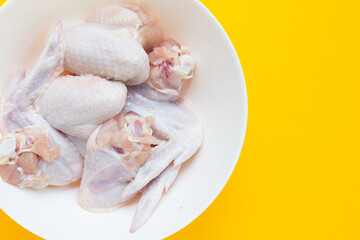 Fresh raw chicken wings in white plate on yellow background.