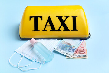 Yellow taxi roof sign, sanitizer, Euro banknotes and medical masks on blue background