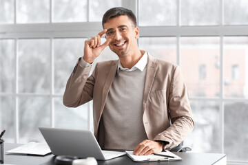 Smiling businessman working with laptop at table in office