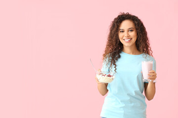 Happy young African-American woman with healthy food on pink background. Diet concept