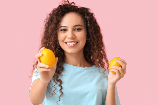 Happy young African-American woman with lemons on pink background