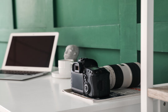 Professional photo camera with magazine on table near green wall, closeup