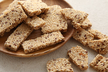 Wooden plate with tasty sesame kozinaki on light background, closeup