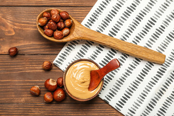 Bowl of tasty nut butter and spoon with hazelnuts on wooden background