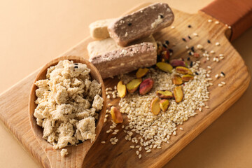 Wooden board of sweet sesame halva with pistachios on color background, closeup