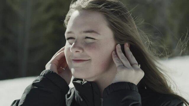 Close up of girl listening to music on earbuds on windy winter day / Tibble Fork, Utah, United States