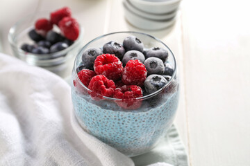 Glass of chia pudding with berries and napkin on white background, closeup
