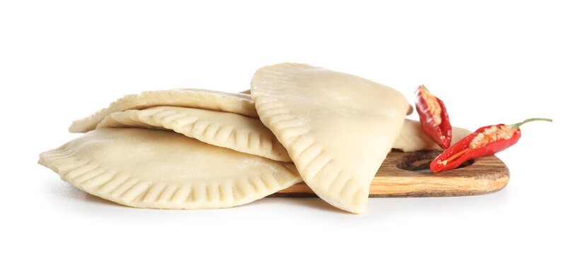 Board with raw chebureks and chili peppers on white background